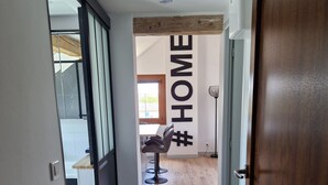A modern interior with a wooden floor, a chair, and a wall with the word "HOME" and a hashtag symbol. - Appartement Sous Combe Climatisé 2 éme Étage (Publier)