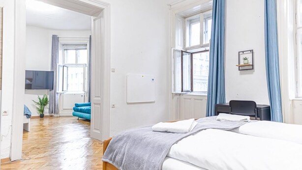 A hotel room with a bed, a desk, a chair, a TV, a plant, and a view of the street. - Family-friendly 2BR Apt.-Perfect for Longstays (Vienna)