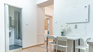 A modern room with a wooden floor, white walls, a white table with four chairs, a whiteboard, and a small potted plant. - Family-friendly 2BR Apt.-Perfect for Longstays (Vienna)