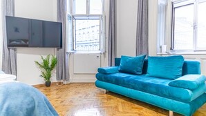 A living room with a blue sofa, a flat-screen TV, a potted plant, and large windows. - Family-friendly 2BR Apt.-Perfect for Longstays (Vienna)