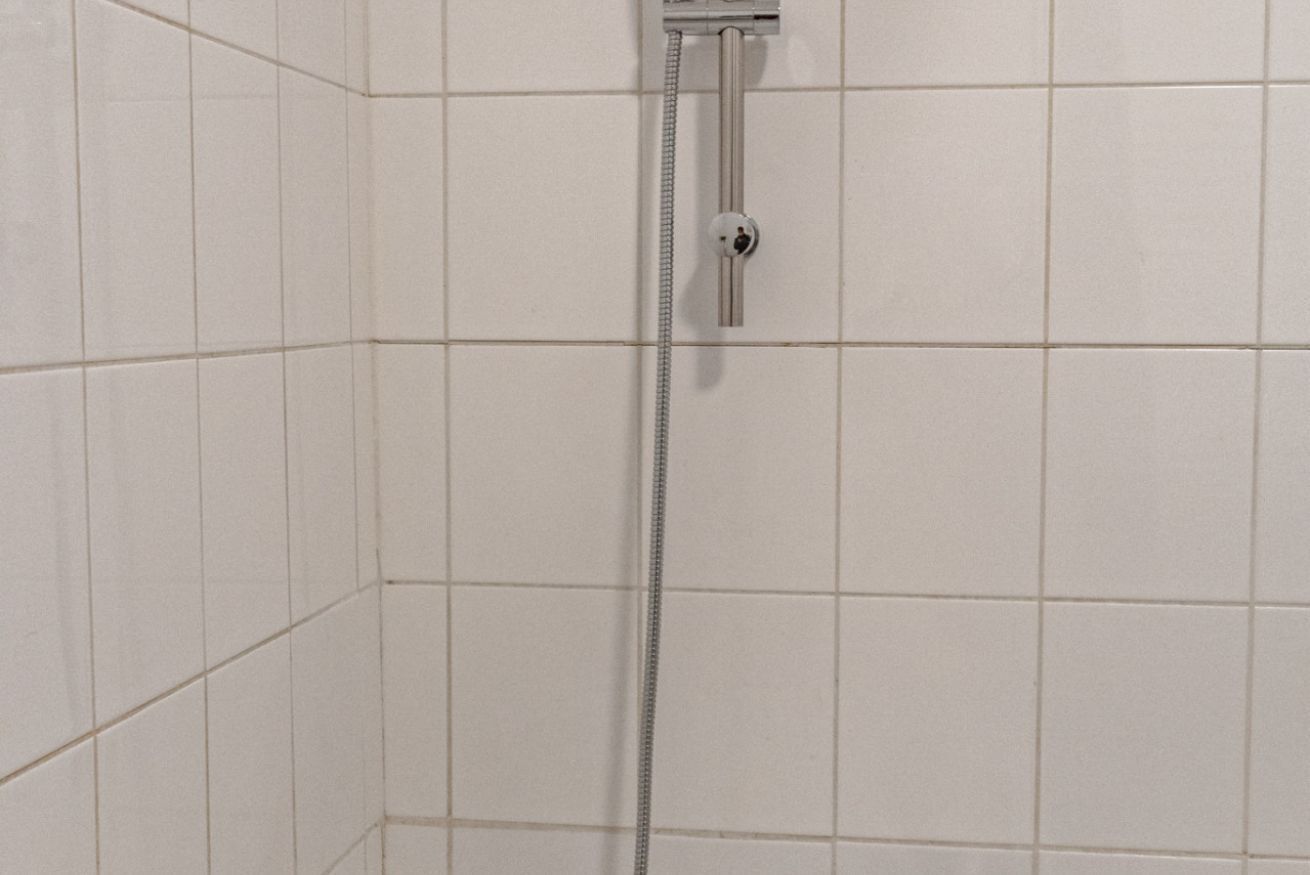 En bruseniche med fliser, et håndholdt brusehoved og en reguleringsknap.