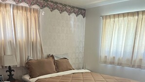 Un dormitorio con cama, mesita de noche, lámpara y cortinas.