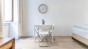 A room with a bed, a table with chairs, a clock on the wall, and a window. - Chic Apartment Suitable for Longstays in Lockdown (Vienna)