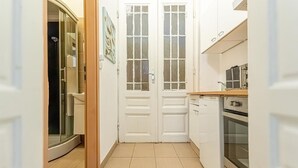 A narrow kitchen with white cabinets, a built-in oven, and a glass shower enclosure. - Chic Apartment Suitable for Longstays in Lockdown (Vienna)