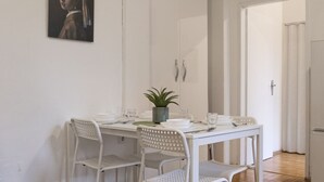 Zona pranzo con tavolo bianco, due sedie, una pianta in vaso e un quadro appeso al muro.