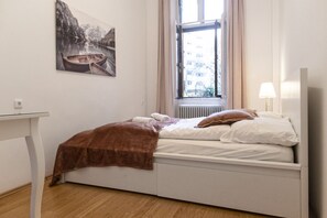 Een slaapkamer met een bed, een raam met gordijnen, een radiator, een tafel en een schilderij aan de muur.