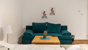 Un salon avec un canapé de couleur turquoise, une table basse en bois agrémentée d’une plante, une lampe blanche et des œuvres d’art abstraites accrochées au mur.