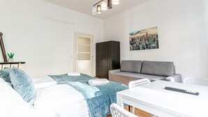 A bedroom with a bed, a grey sofa, a white table, and a painting on the wall.
