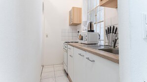 A narrow kitchen with white cabinets, a wooden countertop, a coffee maker, and a window with a view.