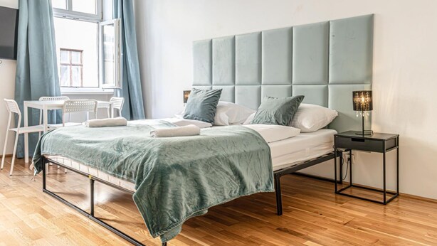 A bedroom with a bed, bedside table, lamp, and a window with curtains.