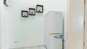 A room with a white refrigerator, a door, and three framed pictures on the wall.
