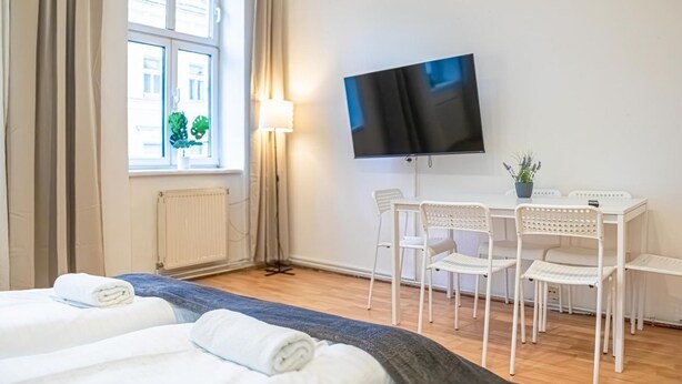 Ein Hotelzimmer mit Bett, Fernseher, Schreibtisch mit Stühlen und einem Fenster mit Vorhängen.
