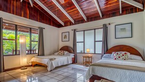 A room with two beds, wooden ceiling beams, large windows with curtains, and a small table with a lamp. - Studio 1 for four to five guests (Parrita)