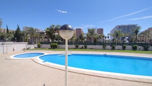 A swimming pool area with two pools, surrounded by a low wall and palm trees.