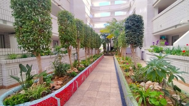A multi-level atrium with a central walkway lined with trees and plants, surrounded by balconies.