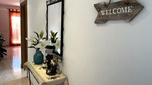 A reception area with a 'WELCOME' sign, a mirror, a table with a vase of flowers, and a plant.