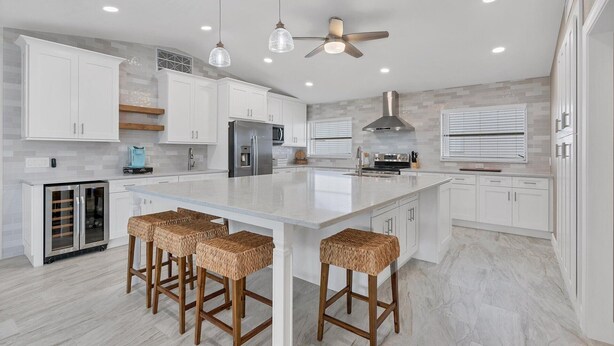 A modern kitchen with white cabinets, a large island with stools, a built-in oven, and a ceiling fan. - 618 via Tunis (Punta Gorda)