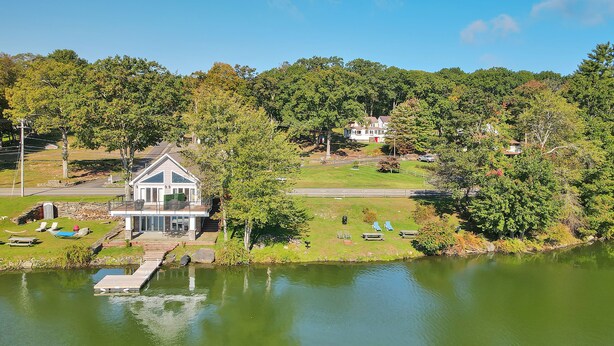 Una casa con muelle junto a un lago, rodeada de árboles y un cielo despejado.