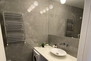 Une salle de bain moderne équipée d’un lave-linge intégré, d’un lavabo avec miroir et d’un porte-serviettes.