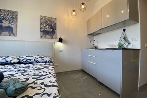 Une pièce de taille modeste comprenant un lit, un coin cuisine et des œuvres d’art accrochées au mur.