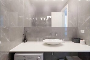 Une salle de bain moderne avec un lavabo blanc, un miroir et un espace douche.