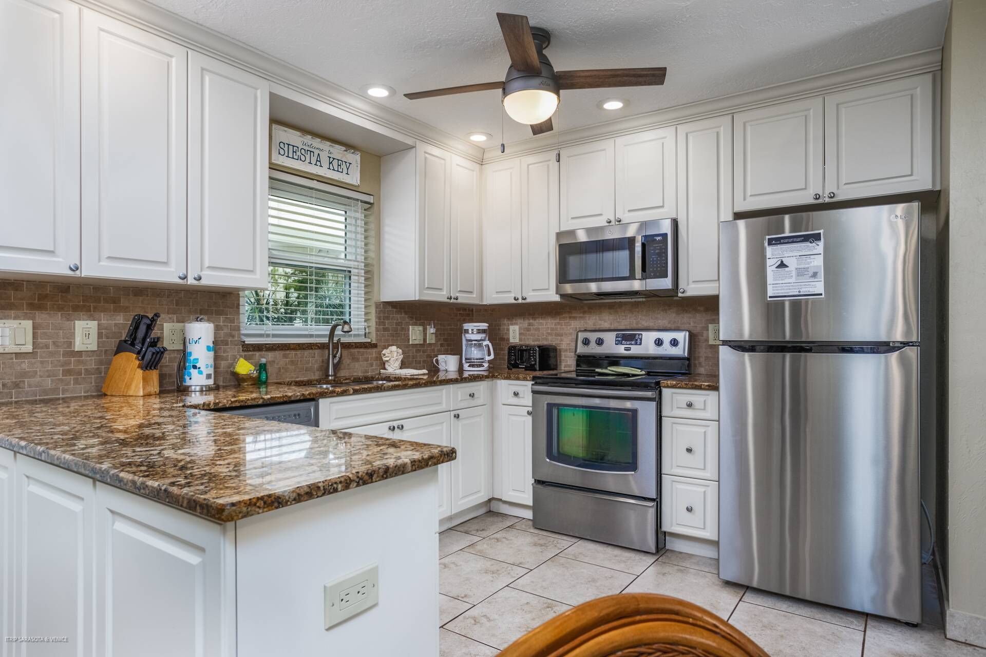 A kitchen with white cabinets, a granite countertop, stainless steel appliances, and a ceiling fan.
