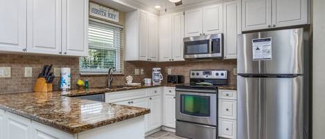 A kitchen with white cabinets, a granite countertop, stainless steel appliances, and a ceiling fan.