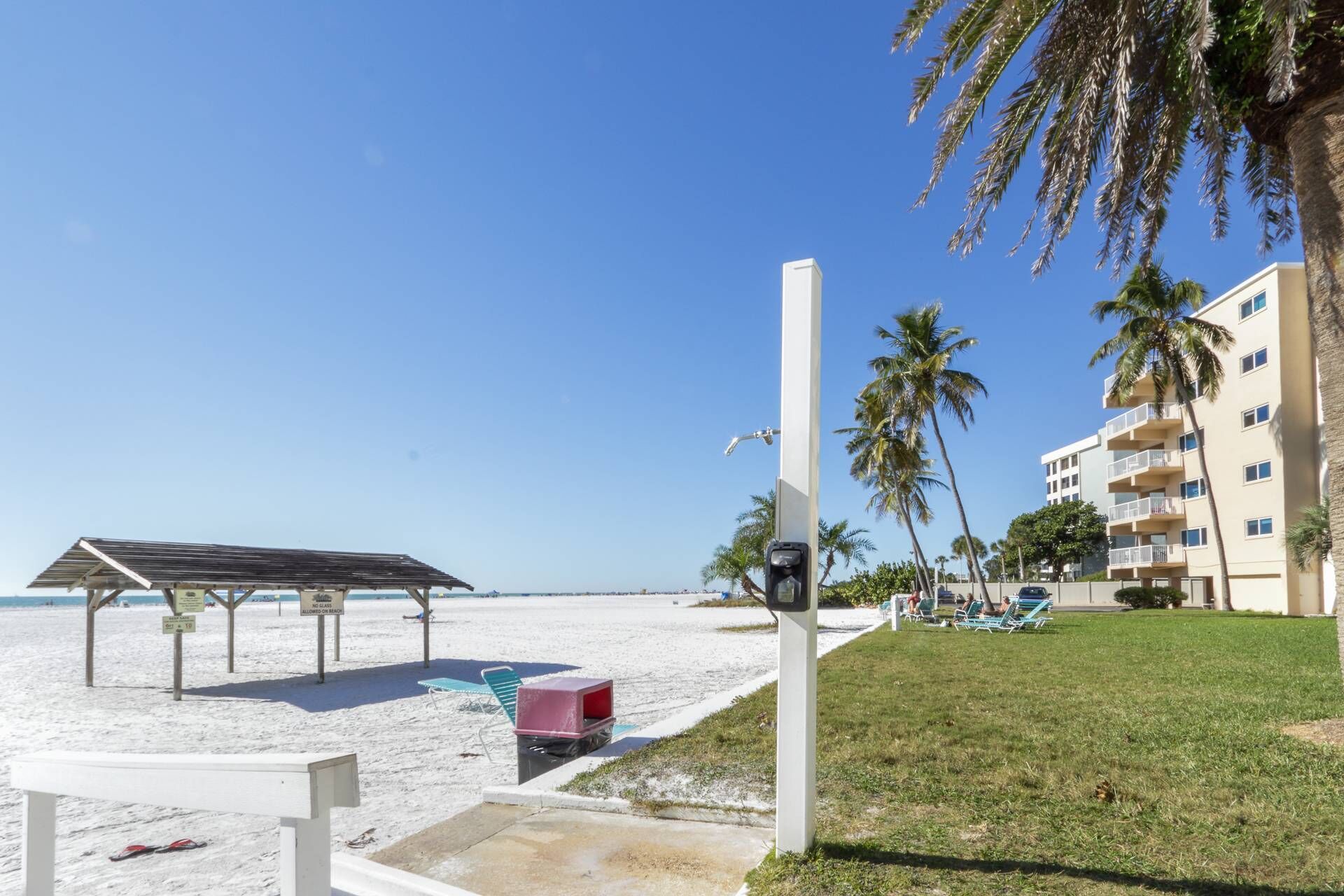 A beach with a covered seating area, a trash bin, and a building with balconies.
