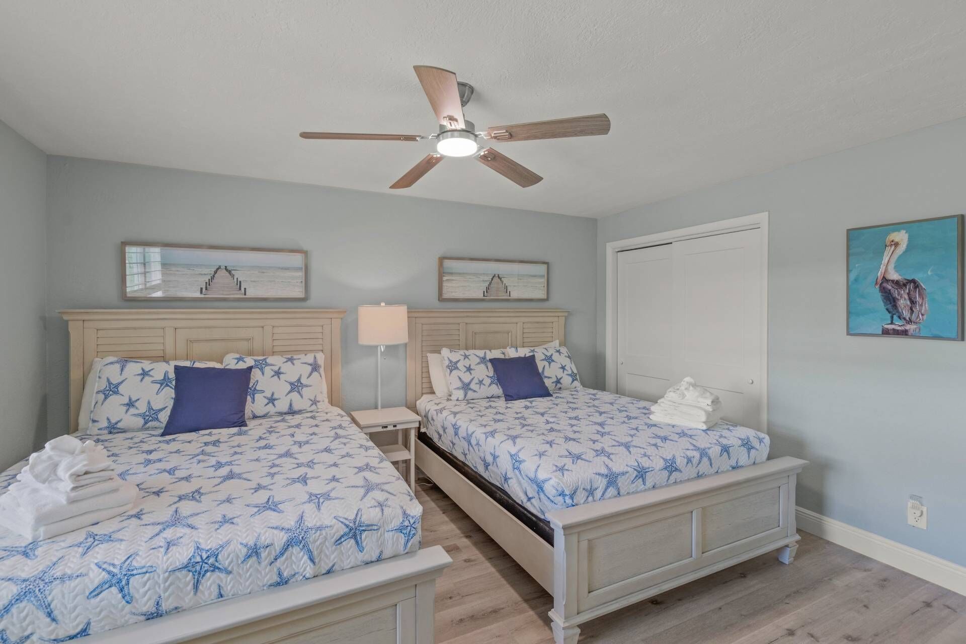 A bedroom with two beds, a ceiling fan, and artwork on the walls.