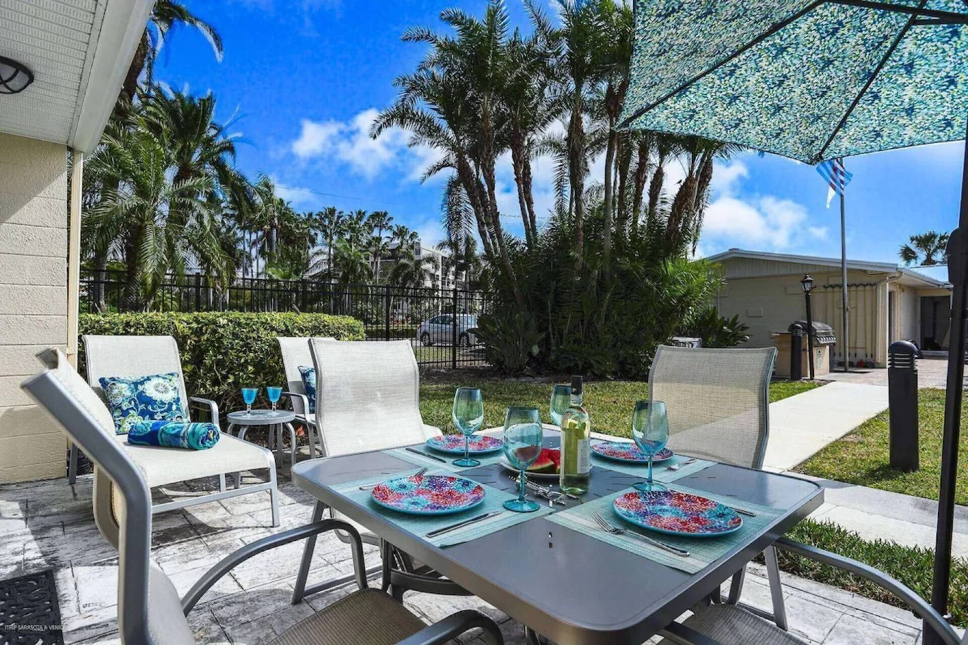 An outdoor patio with a table set for dining, surrounded by chairs and an umbrella.