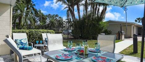 An outdoor patio with a table set for dining, surrounded by chairs and an umbrella.