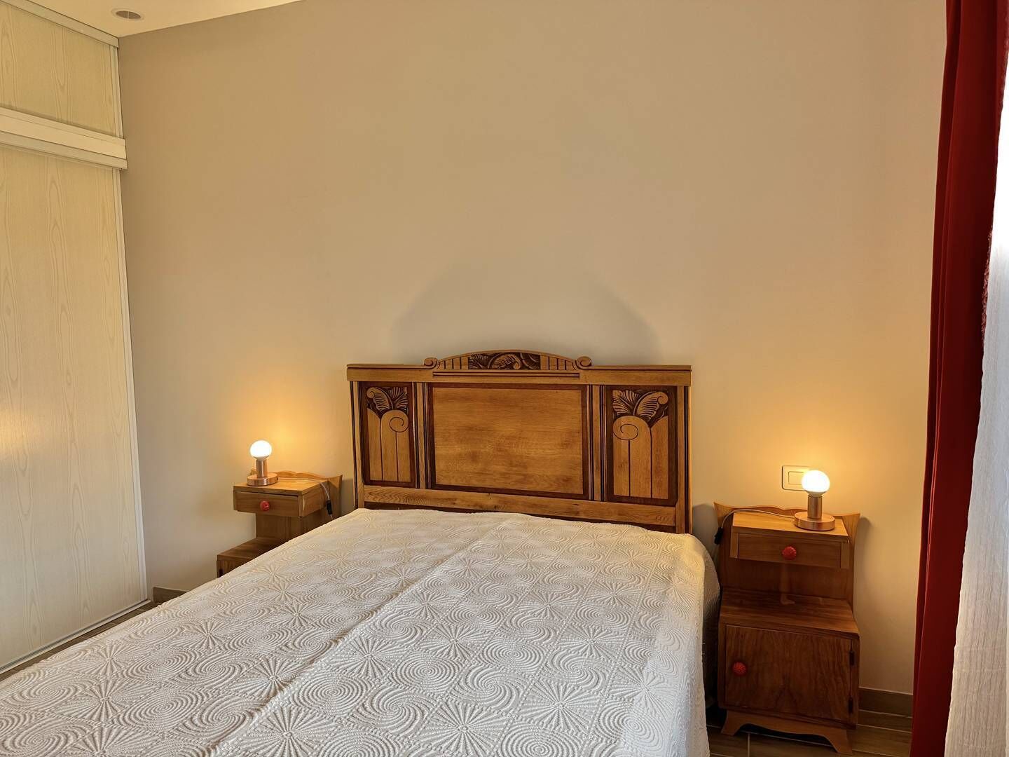 Une chambre à coucher avec une tête de lit en bois, deux tables de chevet avec des lampes et une couvre-lit à motifs.