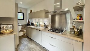Una cocina moderna con estufa a gas, campana extractora de acero inoxidable y horno integrado. Hay un fregadero con grifo y una encimera con diversos electrodomésticos de cocina.