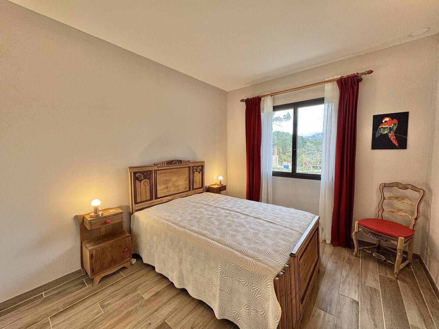 A bedroom with a wooden bed, a nightstand, a chair, and a window with curtains.