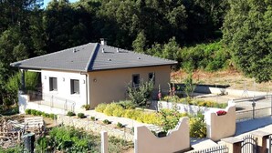 Una casa de una planta con techo de tejas, rodeada de un jardín con diversas plantas y flores.