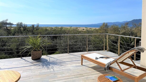 Un balcon doté d’un plancher en bois, d’un fauteuil de relaxation, d’une petite table et d’une plante en pot.