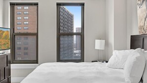 Camera d'albergo con un letto grande, una scrivania e una TV a schermo piatto, oltre a due finestre con vista sugli edifici.