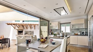 A modern kitchen with white cabinets, a central island, and a dining area with white chairs and a table. - Quinta Valente VIP Properties by Interhome (Silves)