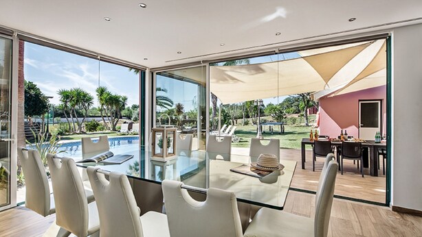 A modern dining area with a glass table and white chairs, overlooking a pool and outdoor seating. - Quinta Valente VIP Properties by Interhome (Silves)