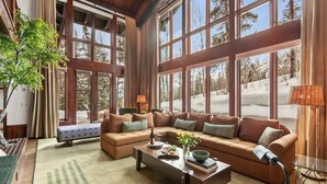 A spacious living room with large windows, a sectional sofa, a coffee table, and a lamp. - Abode on the Big Trail, access to ski runs (Teton Village)