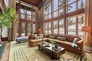 A spacious living room with large windows, a sectional sofa, a coffee table, and a lamp.