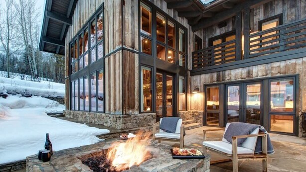 A stone fire pit with a fire, two lounge chairs, and a large wooden building with multiple windows. - Abode on the Big Trail, access to ski runs (Teton Village)