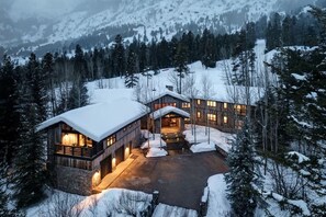 A snow-covered lodge with multiple wooden cabins, a central entrance, and a surrounding forest.