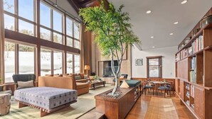 A spacious living area with a large window, a wooden bookshelf, a dining table, and a central plant. - Abode on the Big Trail, access to ski runs (Teton Village)