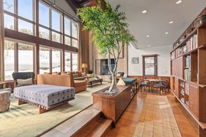 Un vaste espace de vie agrémenté d’une grande fenêtre, d’une bibliothèque en bois, d’une table à manger et d’une plante placée au centre.