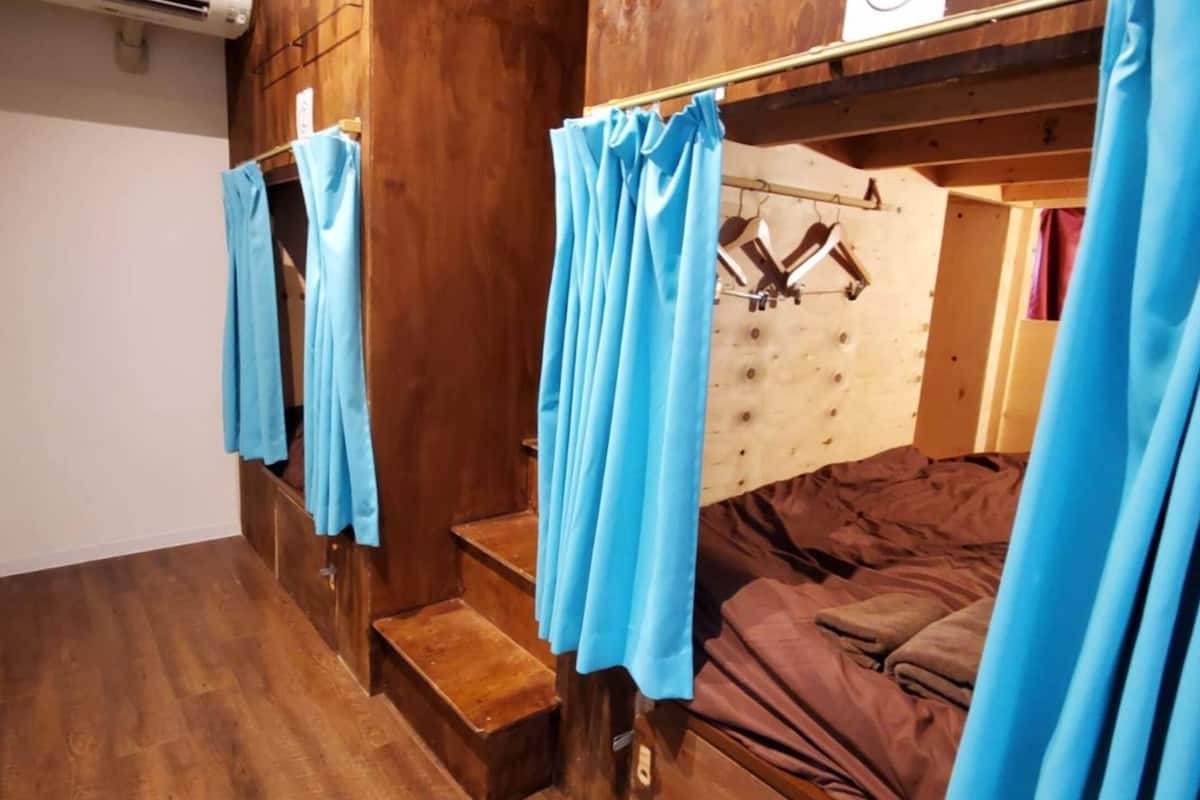 Una habitación tipo cabaña de madera con una cama, un aparador de madera y una ventana con cortinas.