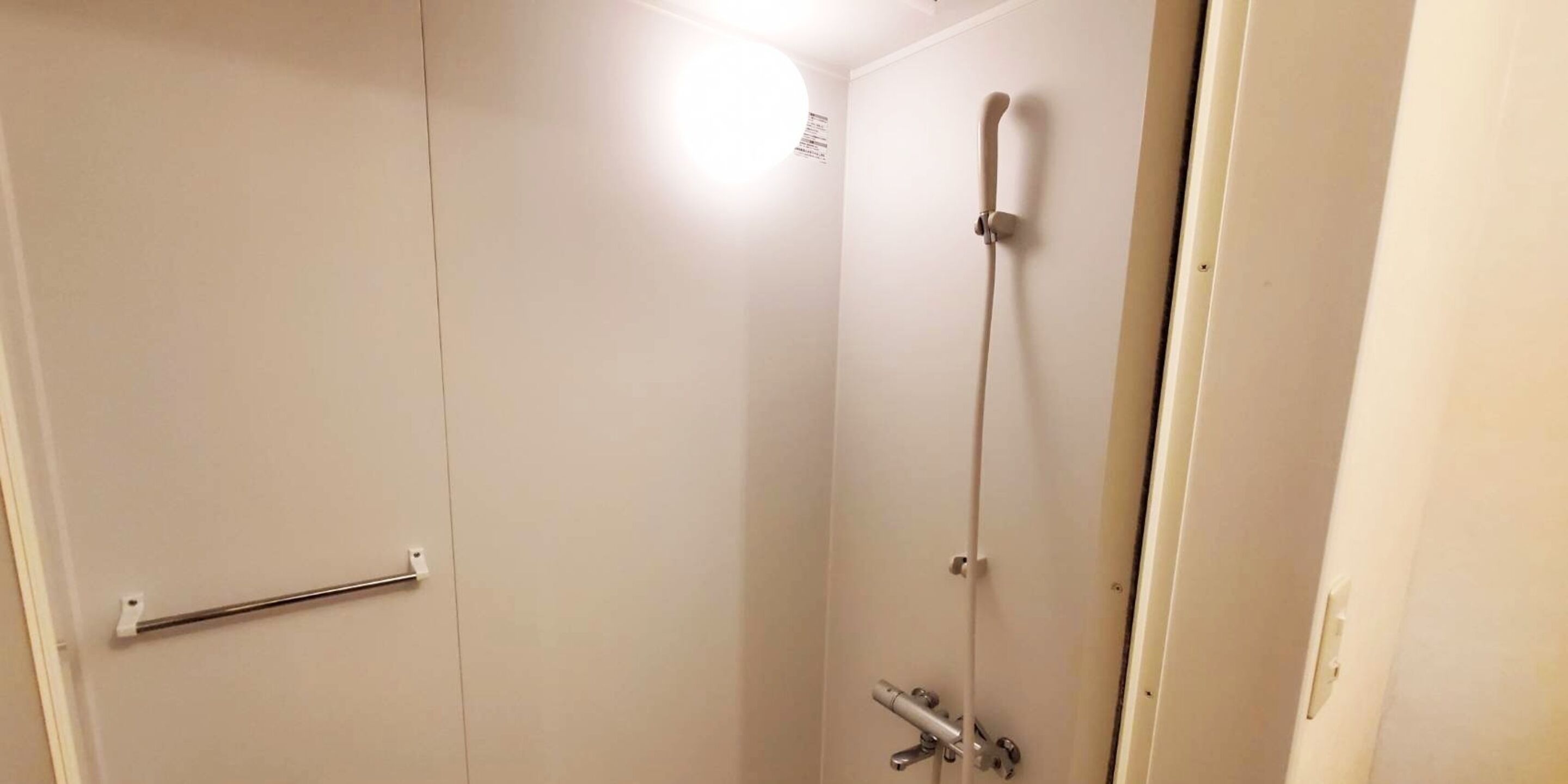 Een kleine, afgesloten douchecel met een handdouche en een kraan op de muur.