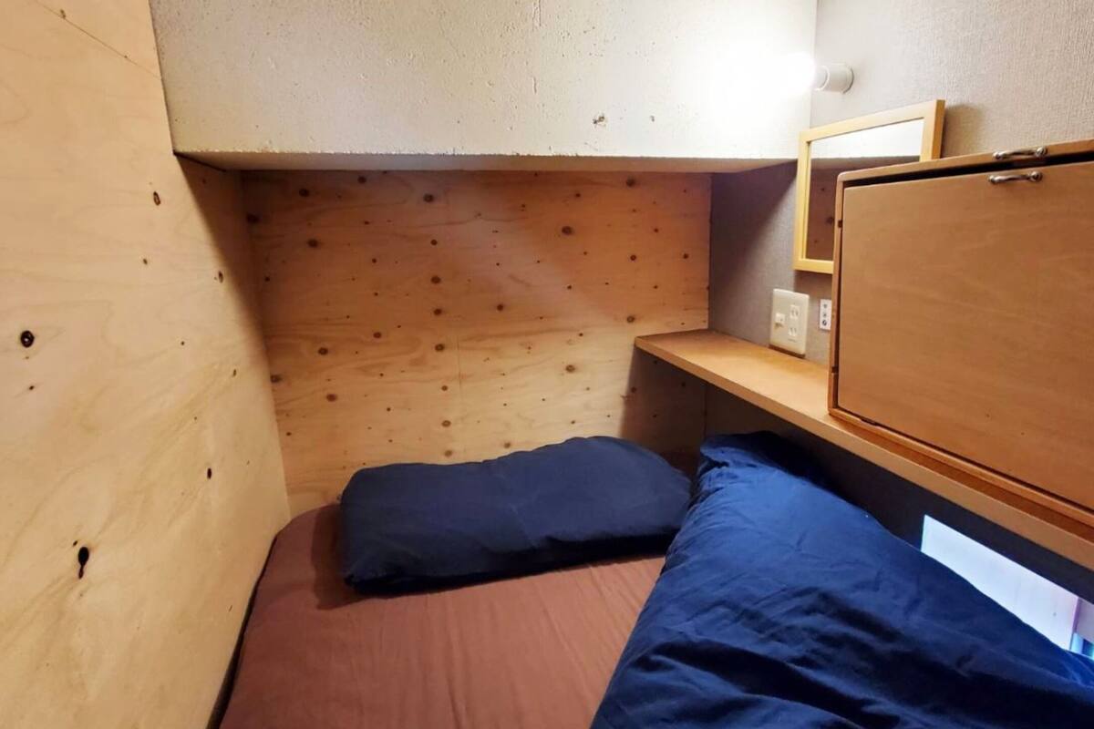 Una habitación pequeña y funcional con una cama nido de madera, una mesita de noche individual y un espejo.