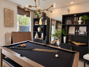 A pool table with a cue stick and balls, a modern chandelier, and a bookshelf with decorative items. - Villa Oasis at Florida. 4 Bed, 3bath 8 People (Homestead)