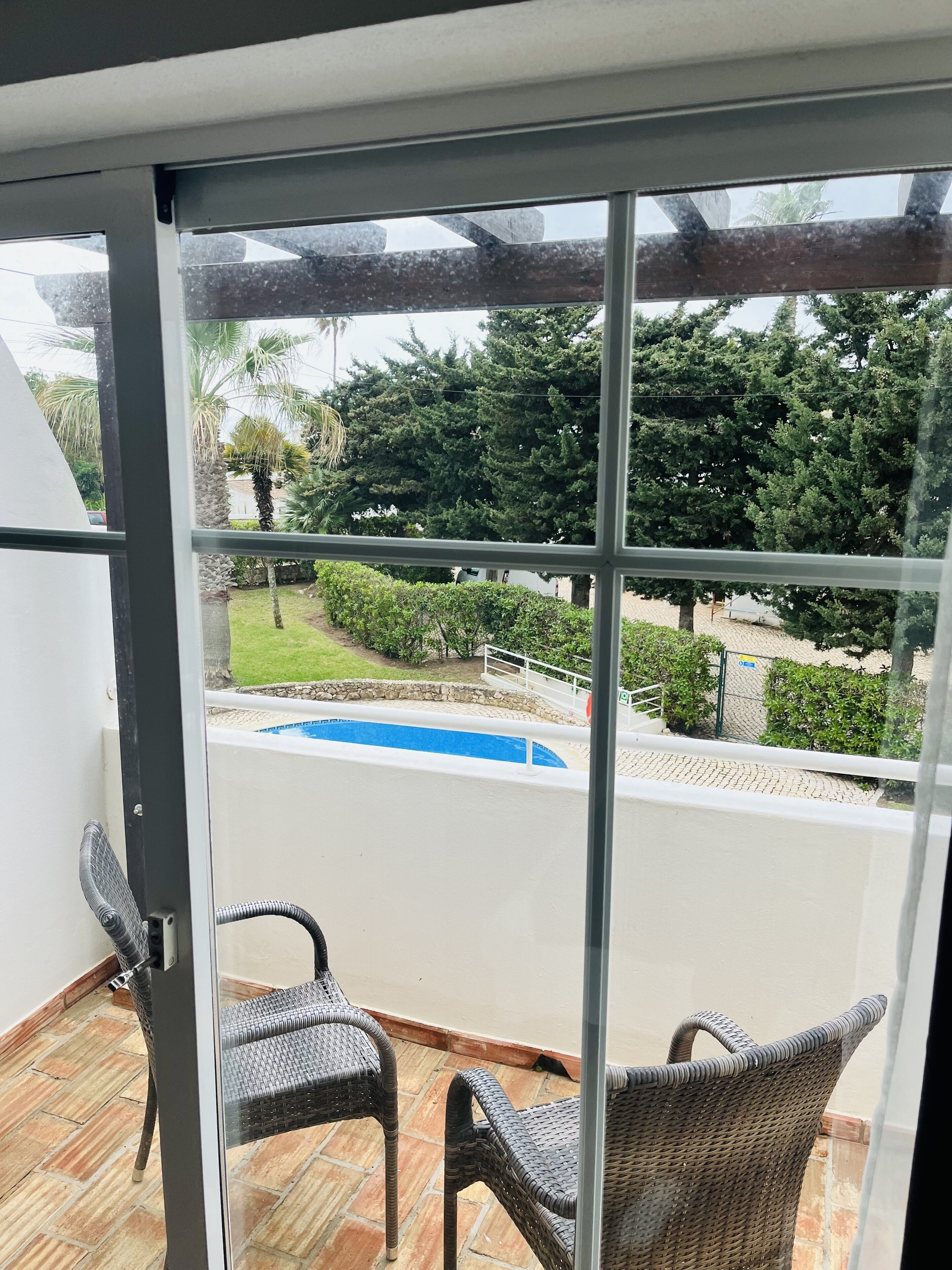 A balcony with wicker chairs, a pool, and a view of greenery and trees.